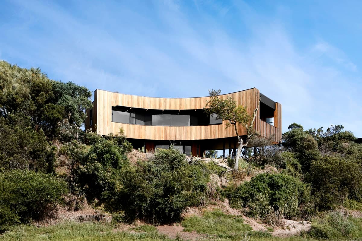 Chic curved modern house on a hillside, seamlessly blending with lush natural surroundings.