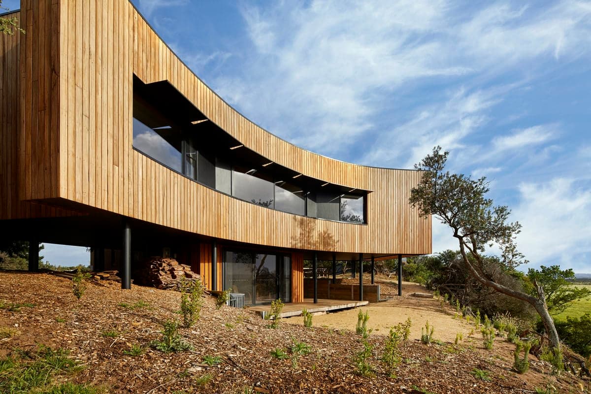 Modern curved wooden house blending seamlessly with nature and picturesque landscape surroundings.