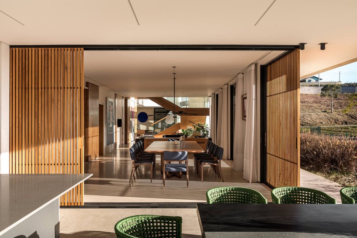 Modern open-plan dining and living space with wooden table, sliding doors, and floating staircase.