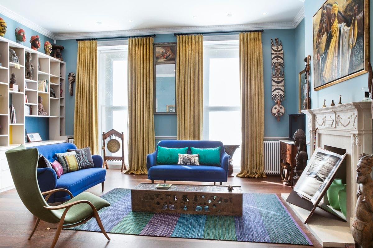 Eclectic living room with blue sofas, gold curtains, and colourful decor.