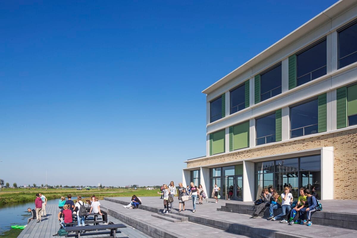 Contemporary three-story educational building with large windows, stepped patio, and green lawn.