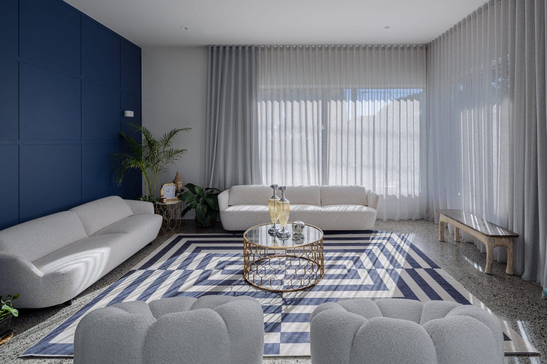 Modern living room with white, blue, and grey decor, featuring plush sofas and a glass coffee table.