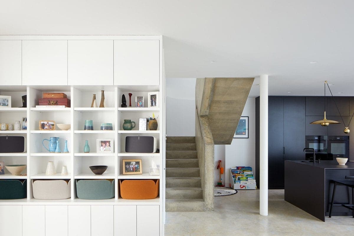Modern, minimalistic family home with concrete staircase, sleek kitchen, and organized shelving.