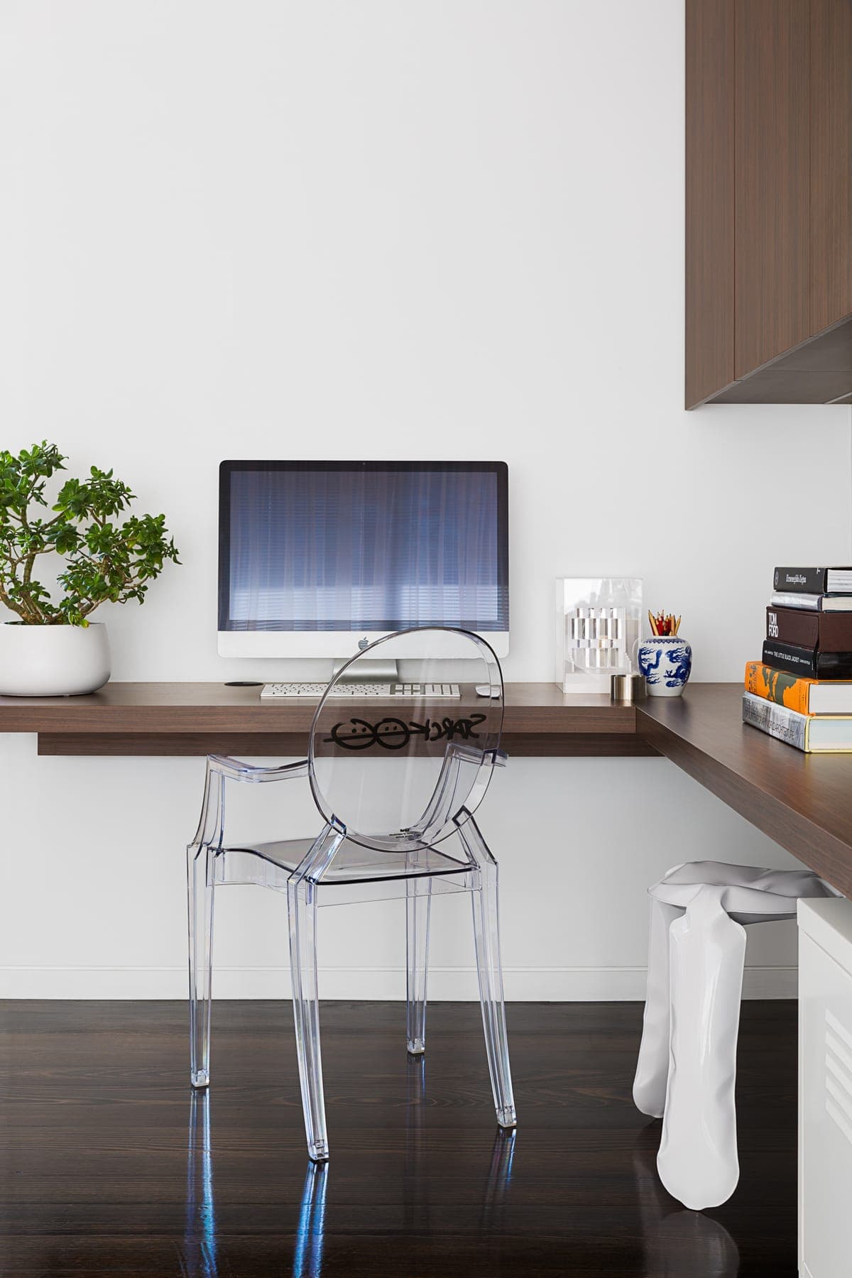 Minimalist modern home office with floating desk, computer, plant, and transparent chair.
