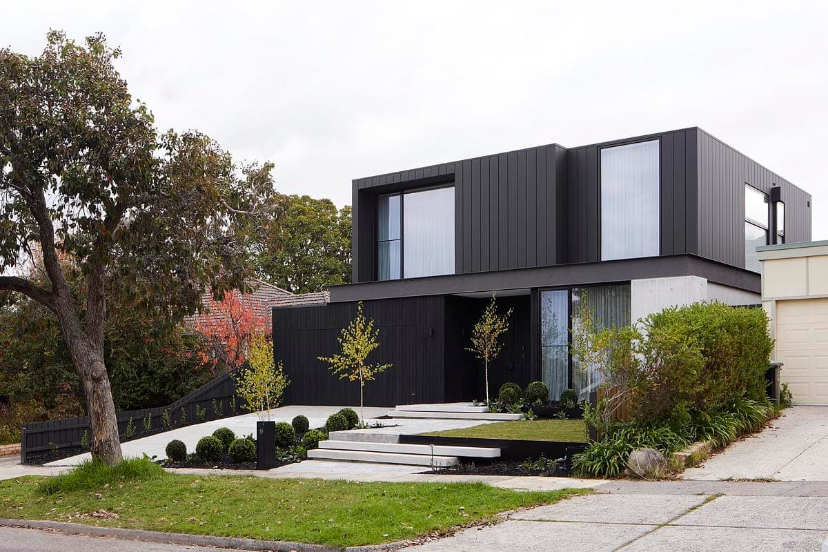 Sleek contemporary black-clad home set amid stylish landscaping and panoramic windows.