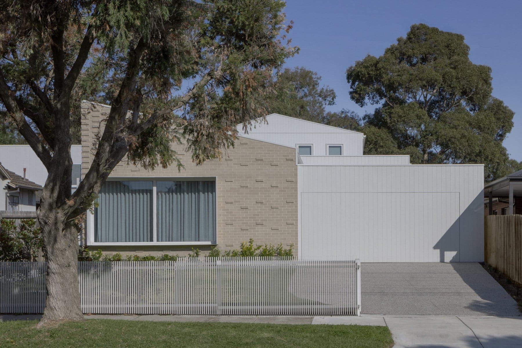 Modern single-story house with minimalist design, light bricks, white panels, and landscaped front yard.