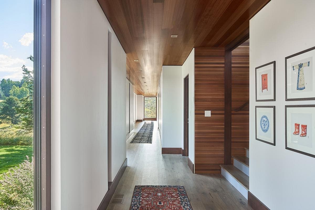 Stylish corridor with large windows, warm wood accents, and art, enhancing modern interior design.