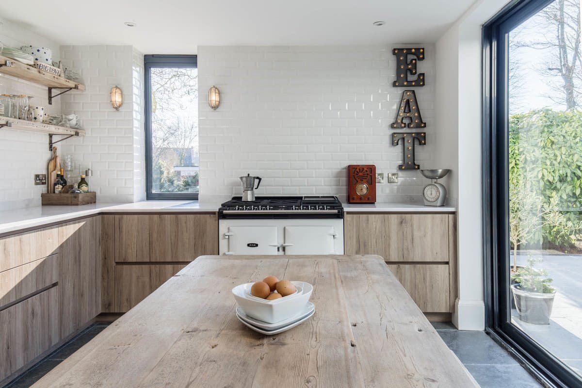 Modern U-shaped kitchen with rustic dining table, light wooden cabinetry, and white subway tile backsplash.