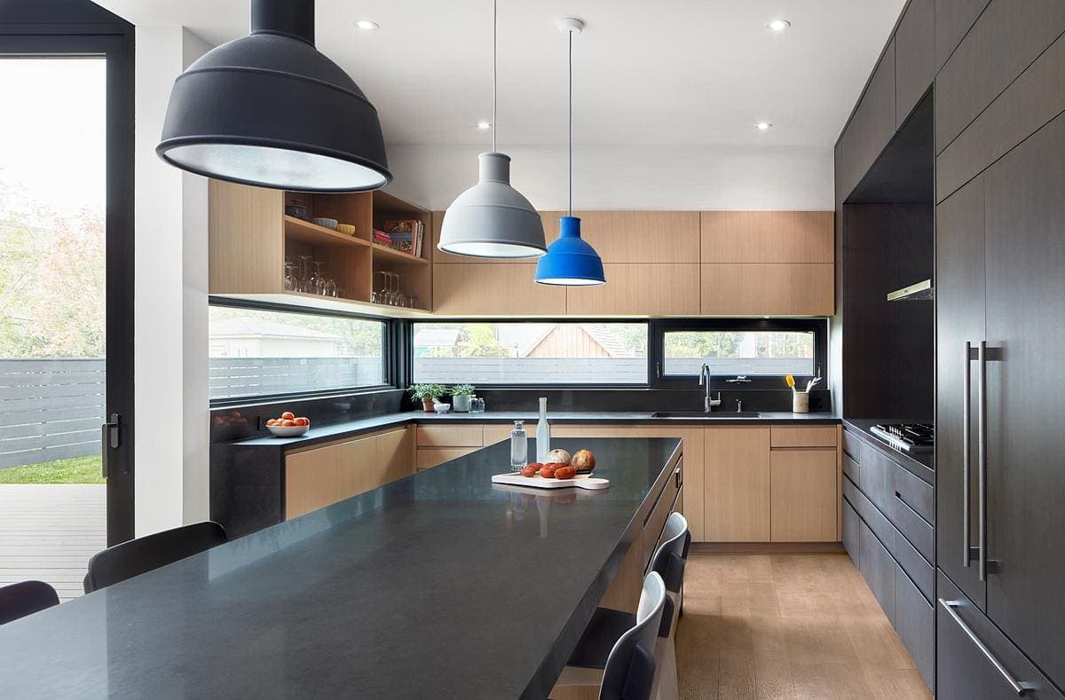 Modern kitchen with black and wood tones, sleek island, pendant lights, and large window.
