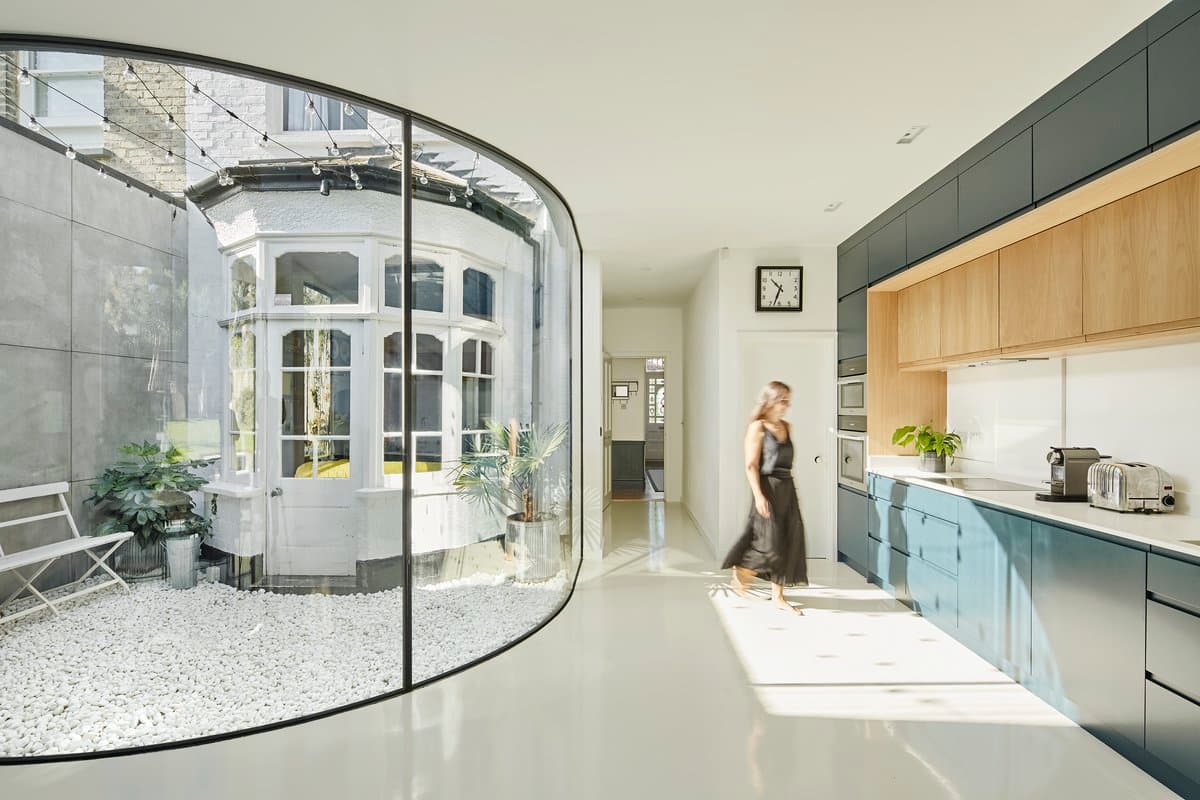 Modern kitchen with curved glass wall and outdoor courtyard.