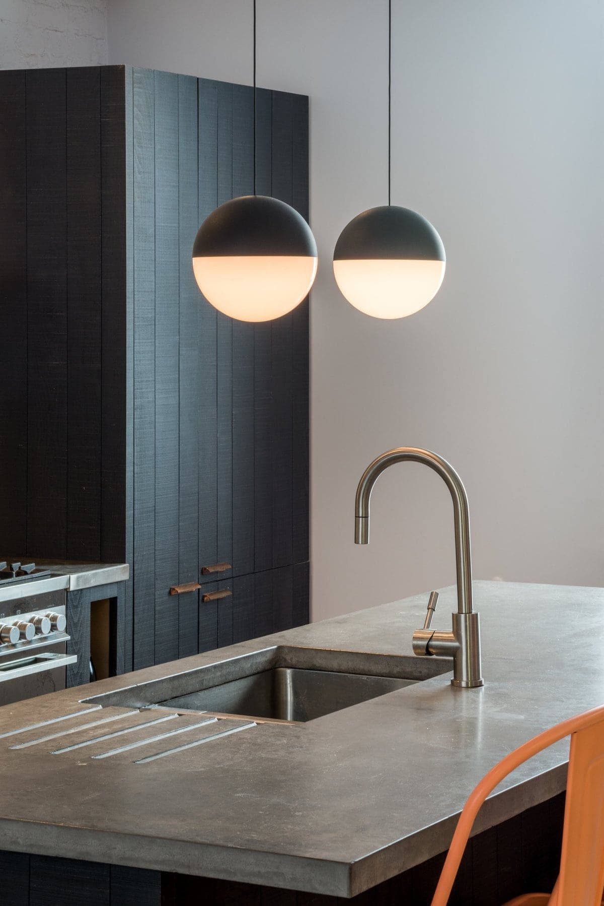 Modern kitchen with grey concrete countertop, pendant lights, dark wood cabinet, and orange chair.