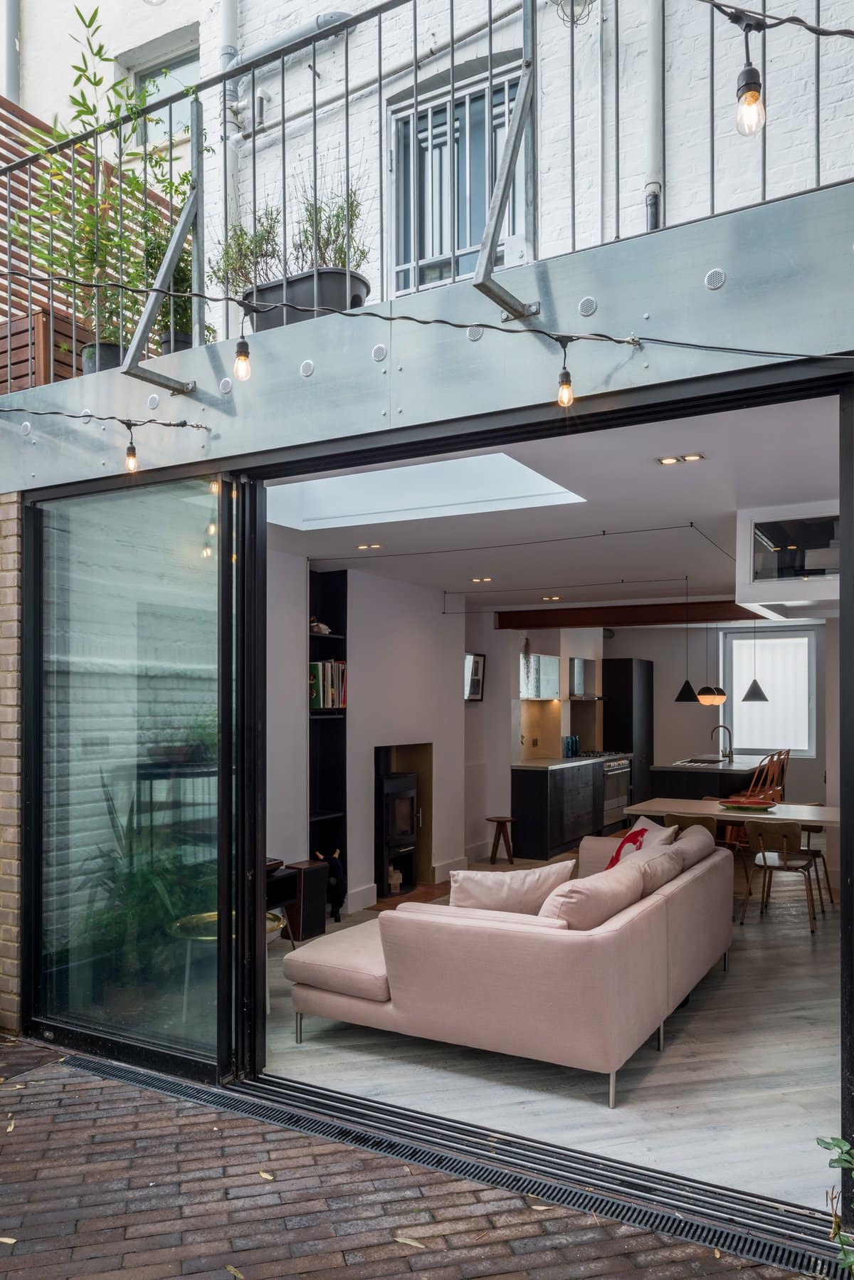 Modern living area with open glass doors, pink sofa, dining area, and outdoor brick paving.