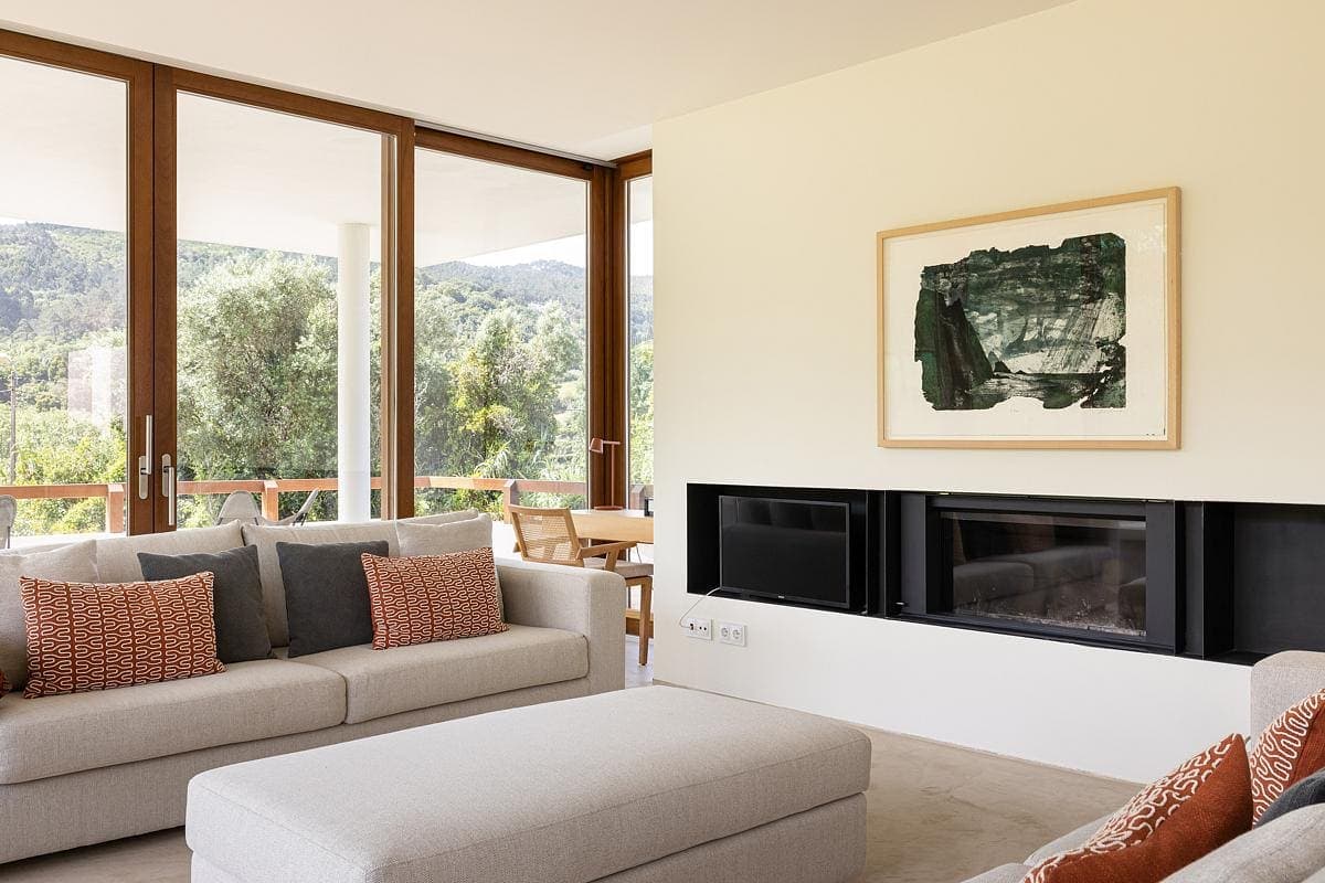 Modern minimalist living room with natural light, lush views, and contemporary decor.