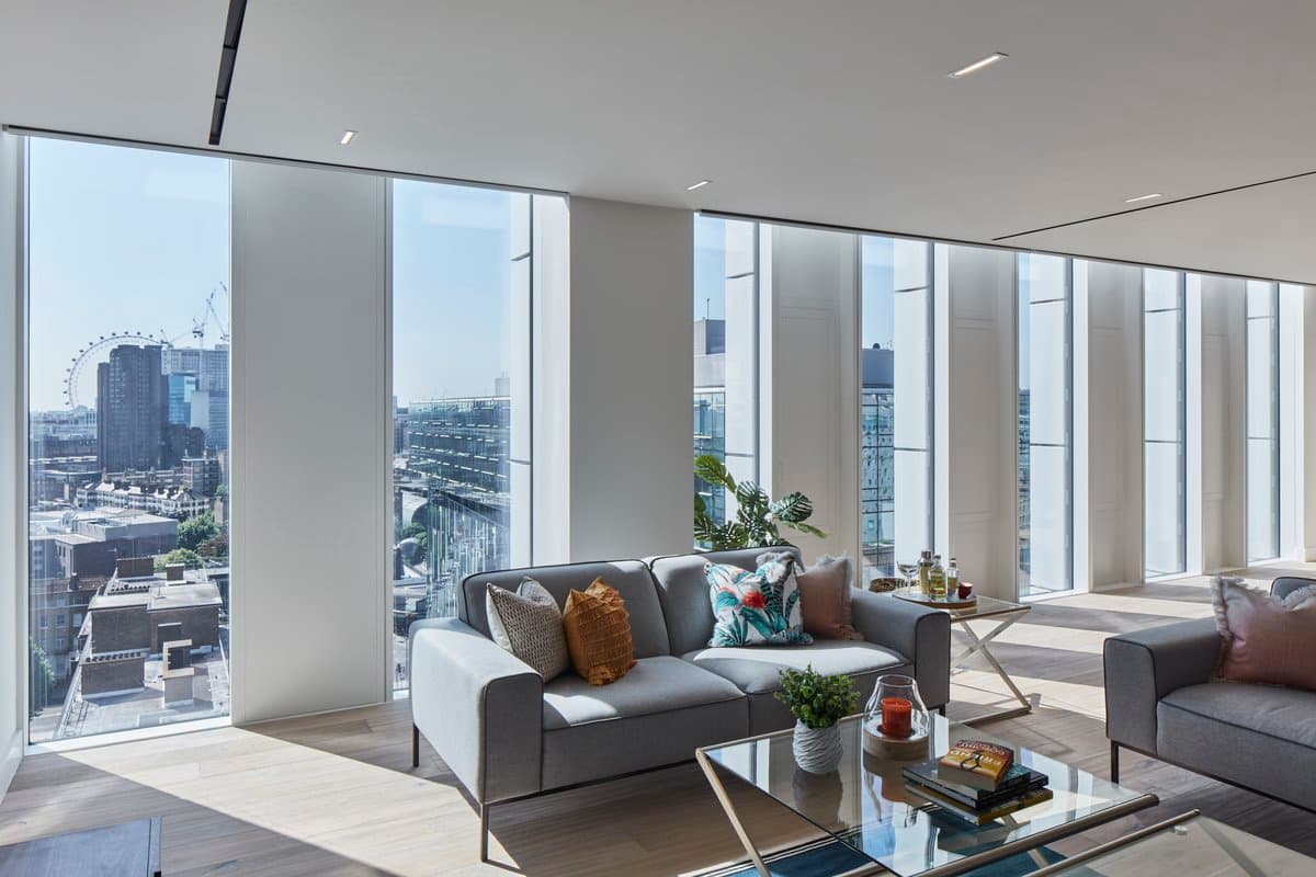 Modern luxury living room with city skyline views, grey sofas, glass coffee table, and natural light.