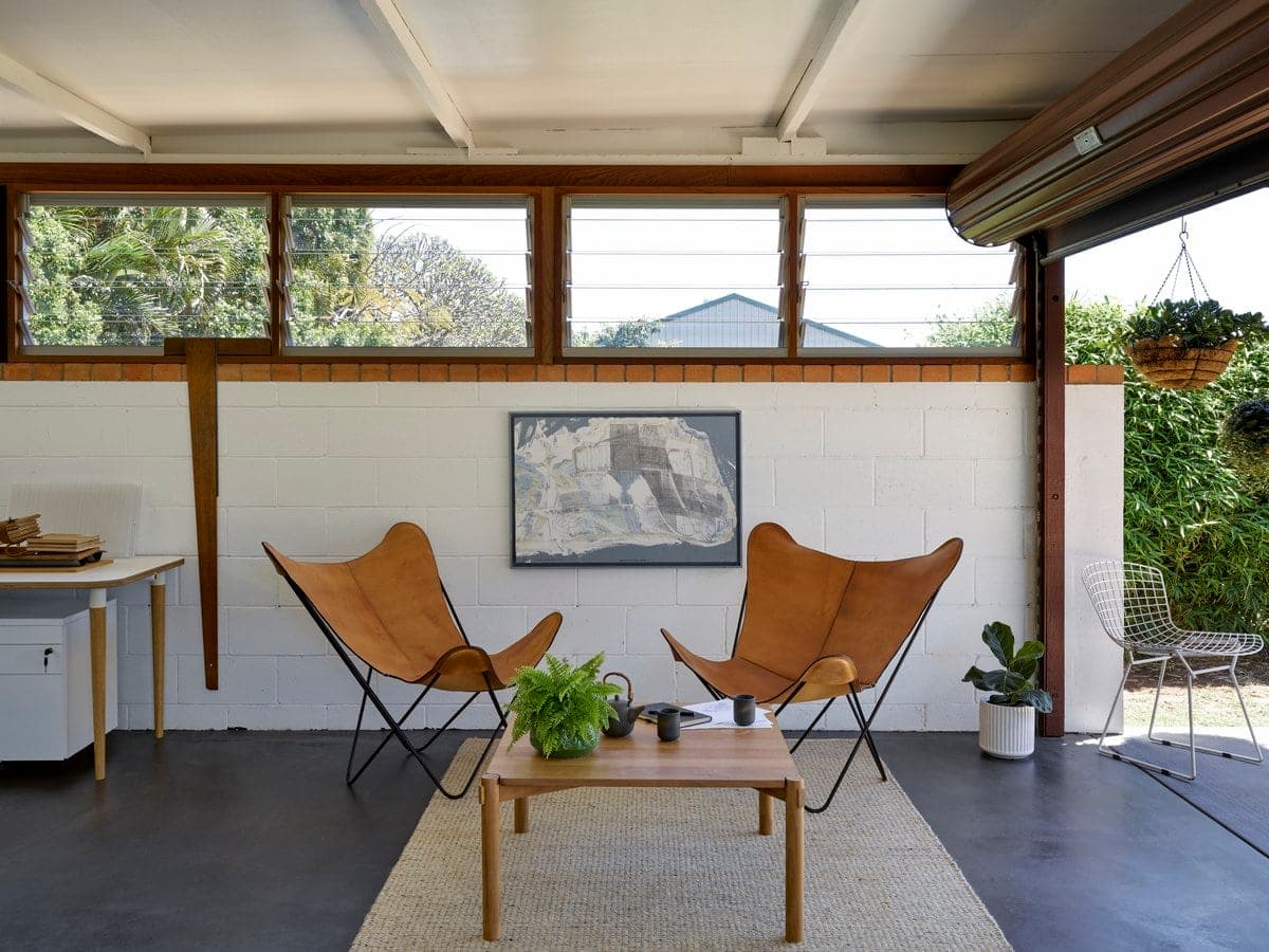 Modern minimalist indoor space with butterfly chairs, coffee table, and natural light from windows.