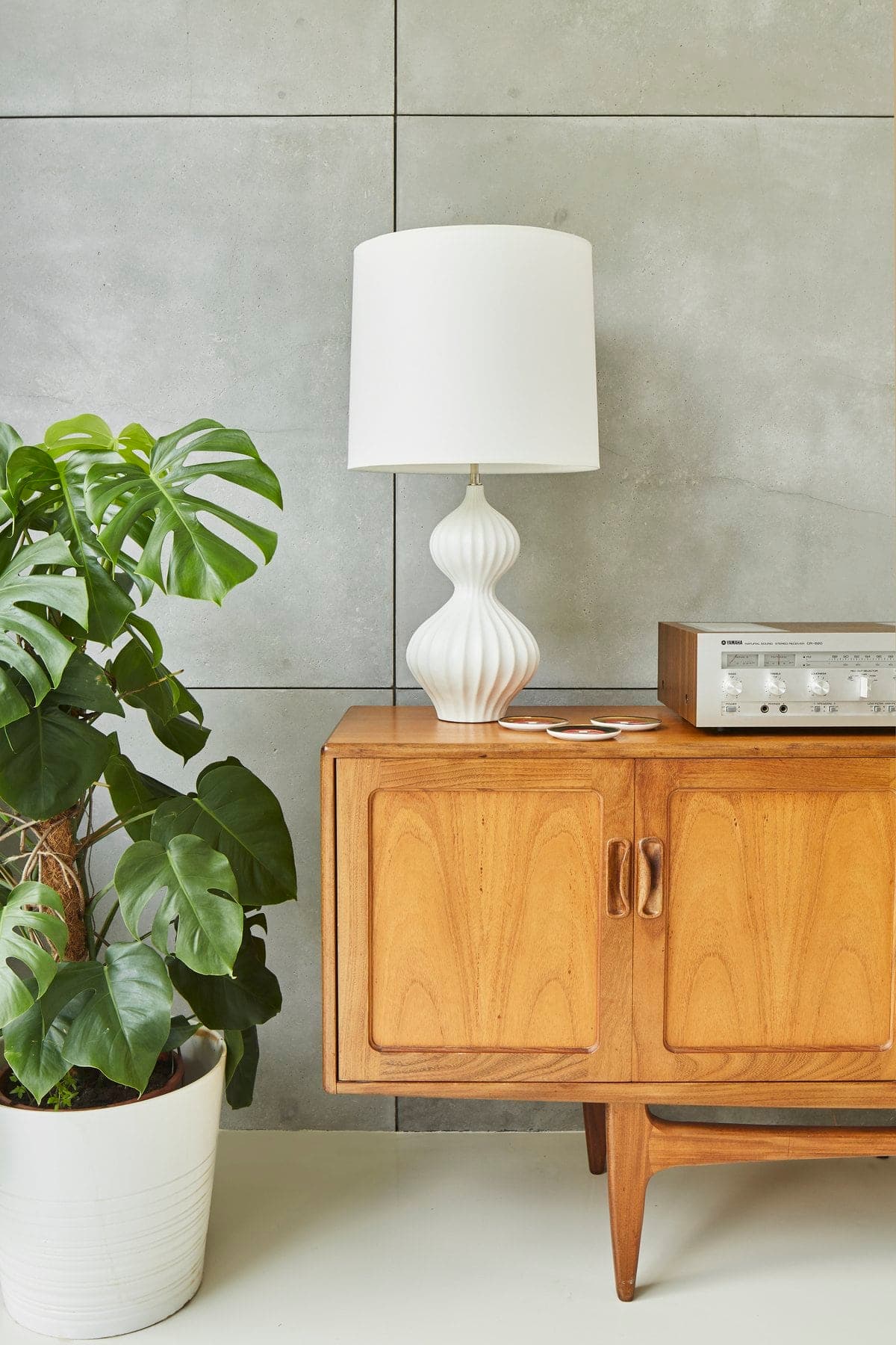 Modern minimalist interior with wooden cabinet, vintage radio, potted plant, white lamp, and grey tiled wall.