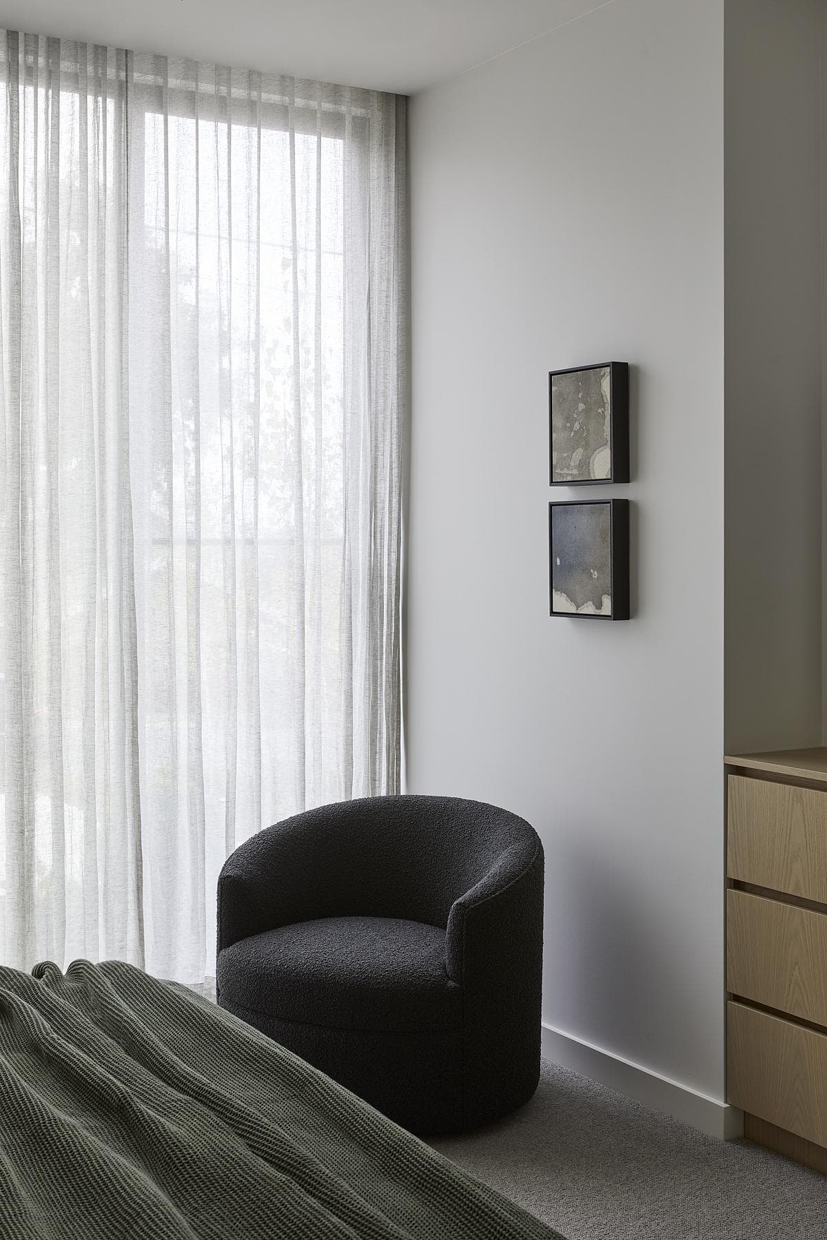 Stylish minimalist bedroom featuring a cozy black armchair and soft natural light.