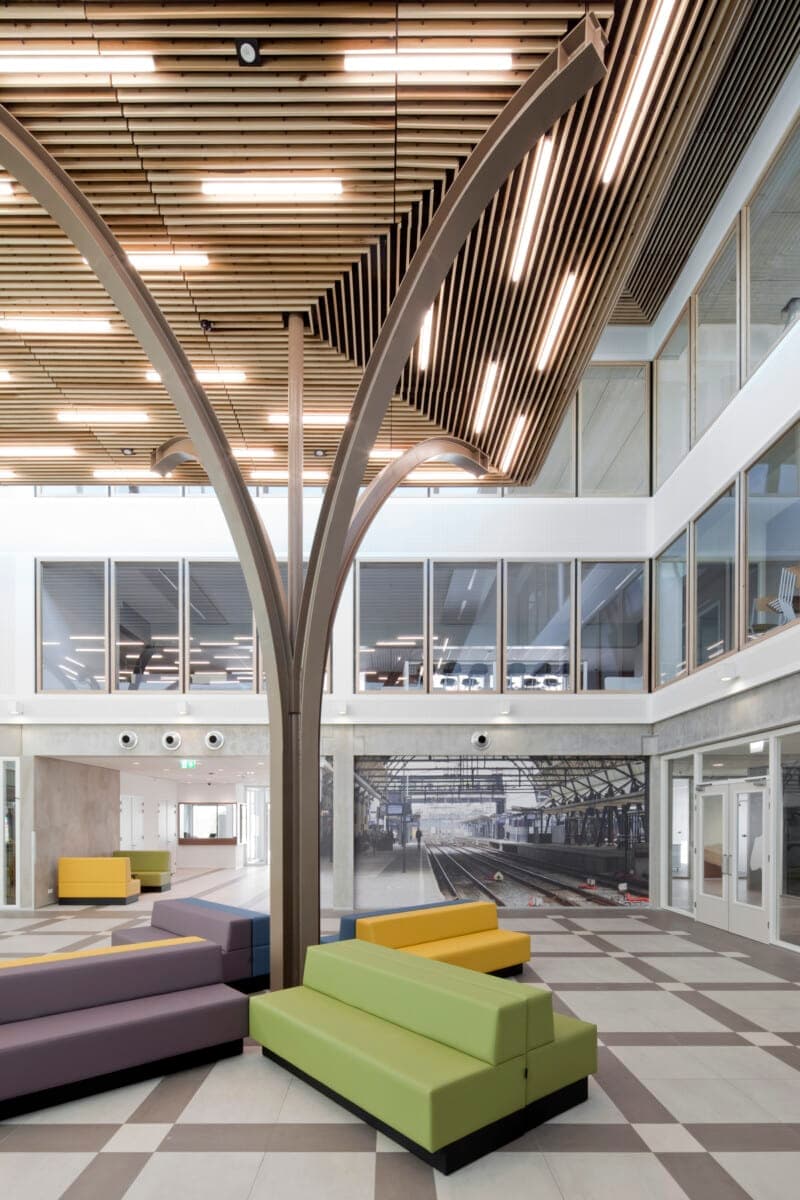 Modern open-concept interior with tree-like column, wooden ceiling, modular seating, and large windows.