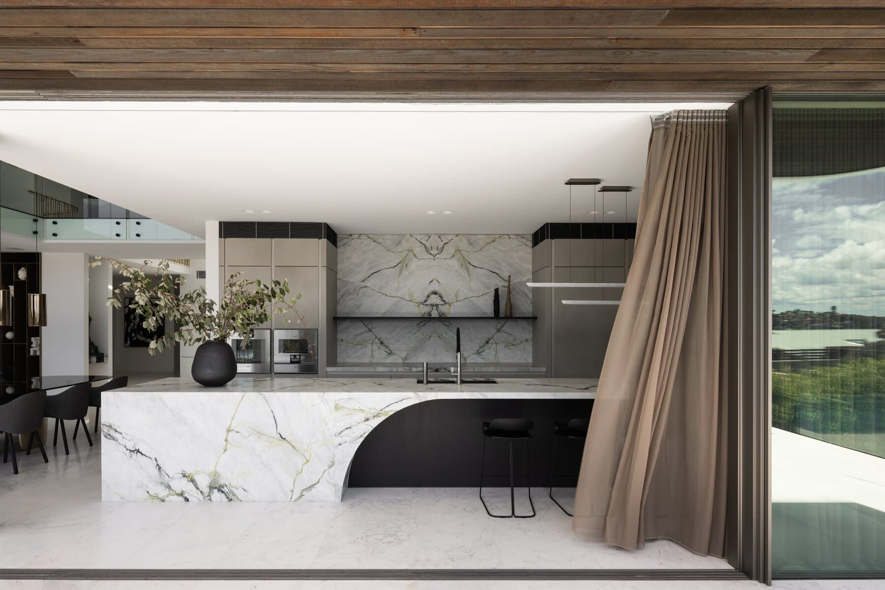 Modern open-concept kitchen with marble island, black faucet, pendant lights, and natural lighting.