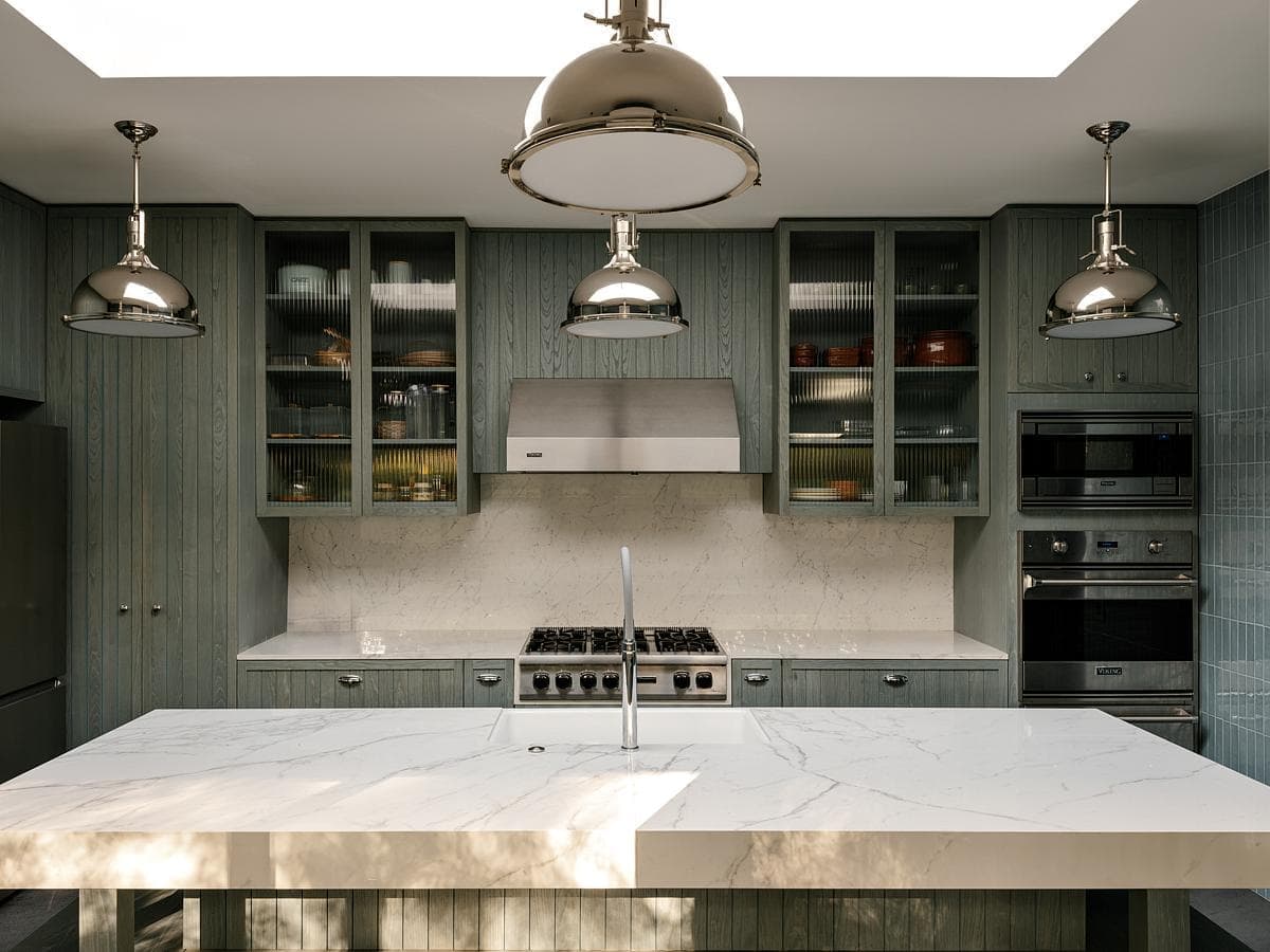 Modern kitchen with green cabinetry, marble island, and stylish pendant lighting.