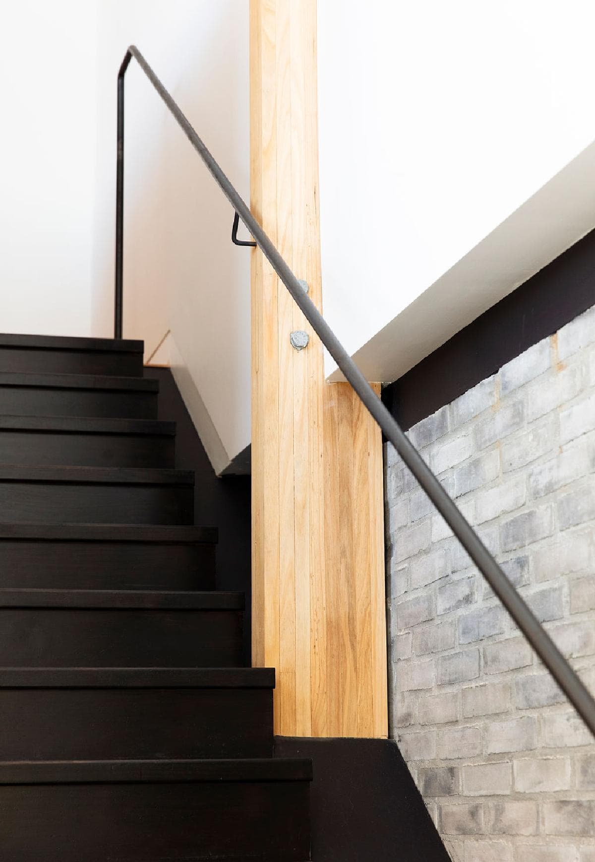 Sleek modern staircase blending dark metal and warm wood with exposed brick accents.