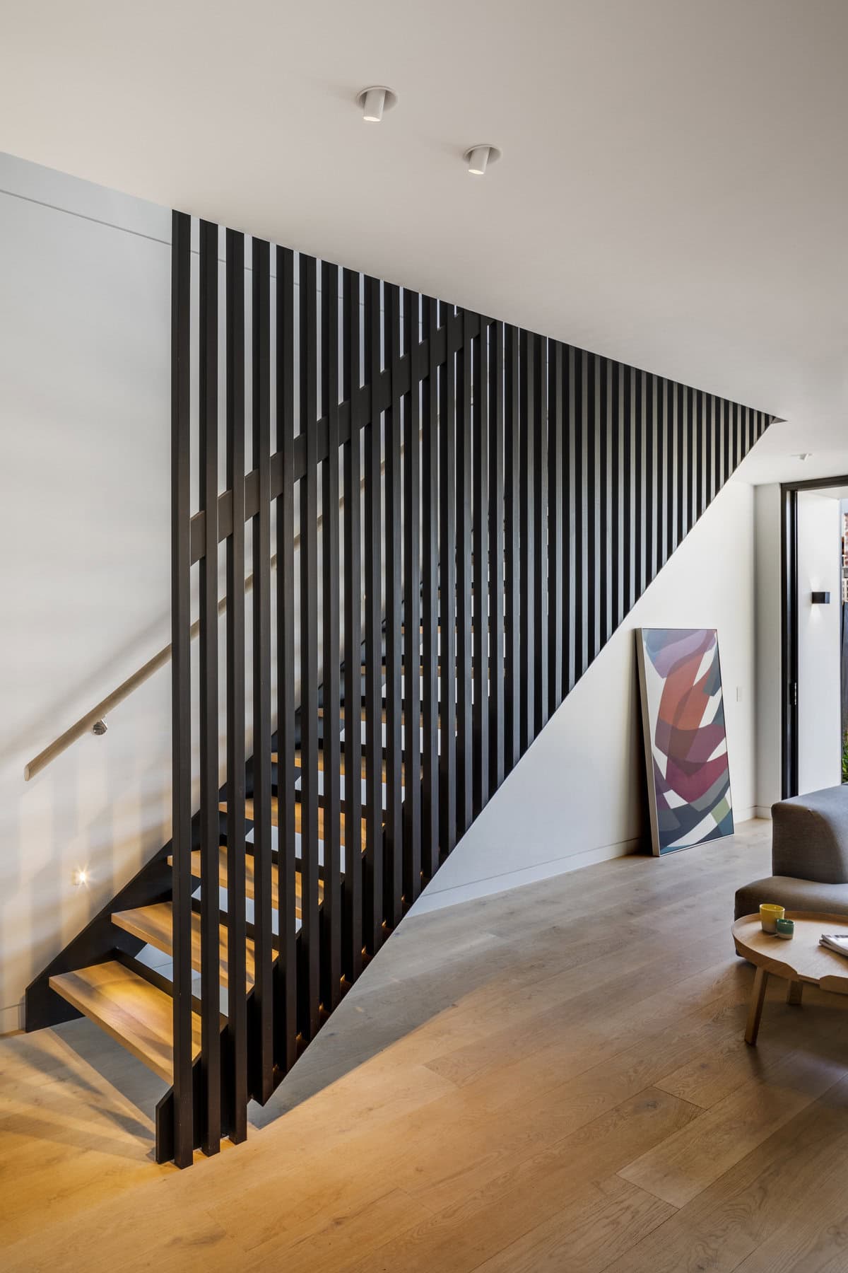 Contemporary wooden staircase with metal railing and artwork, blending style and functionality.
