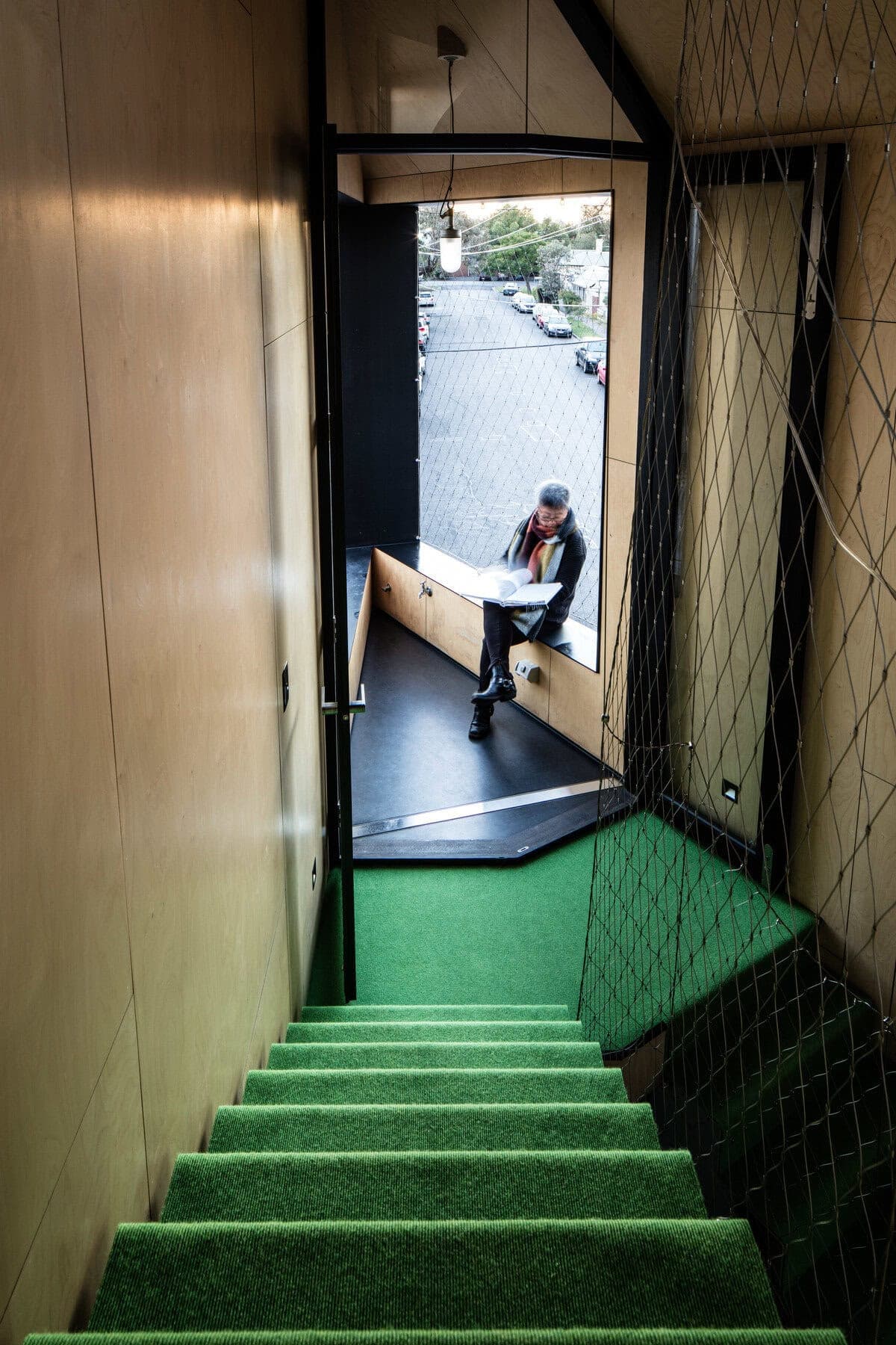 Modern staircase leading to a cozy urban reading nook with large windows and natural light.