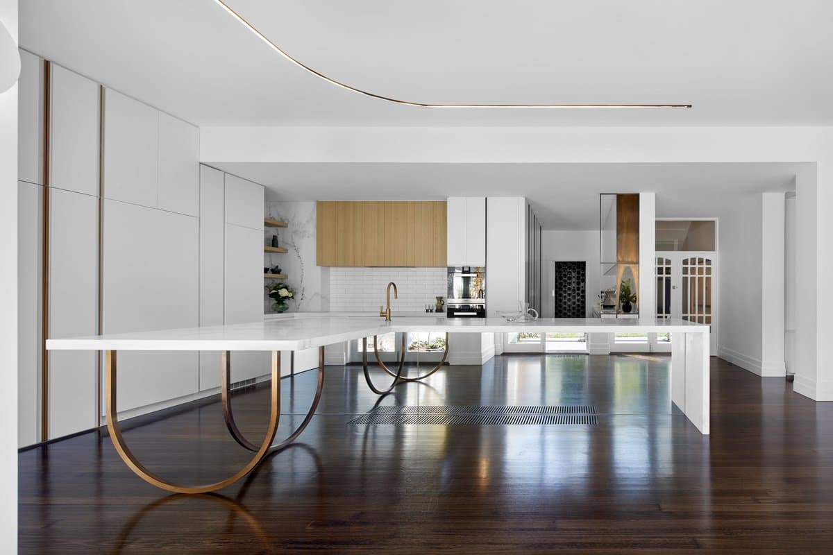 Modern white kitchen with marble island, gold accents, light wood cabinetry, and dark wood flooring.
