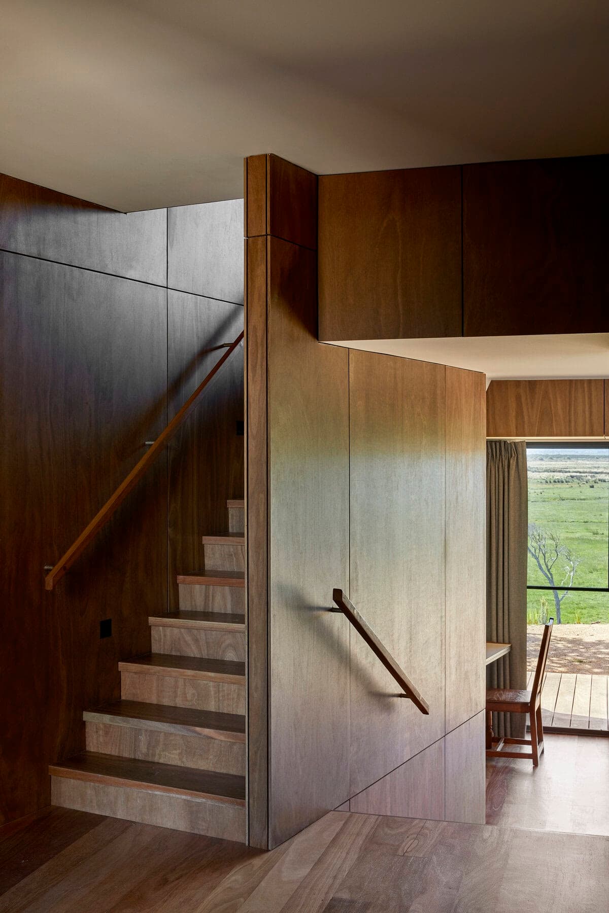 Contemporary wooden staircase bathed in natural light, offering serene outdoor views and inviting warmth.