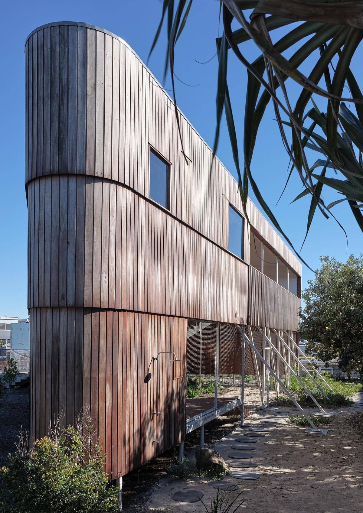Timber-clad house with large windows among trees and planting.