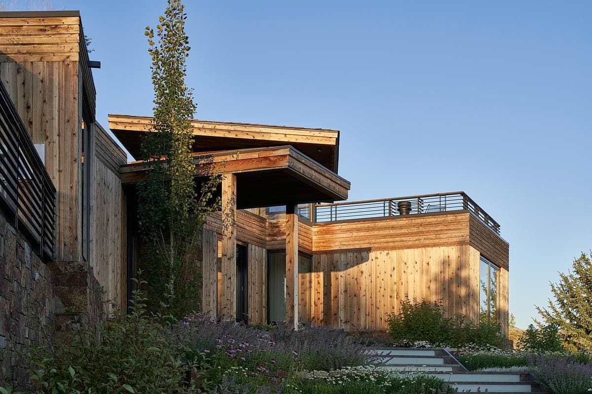 Contemporary wooden house in a serene hillside setting with lush landscaping and a rooftop terrace.