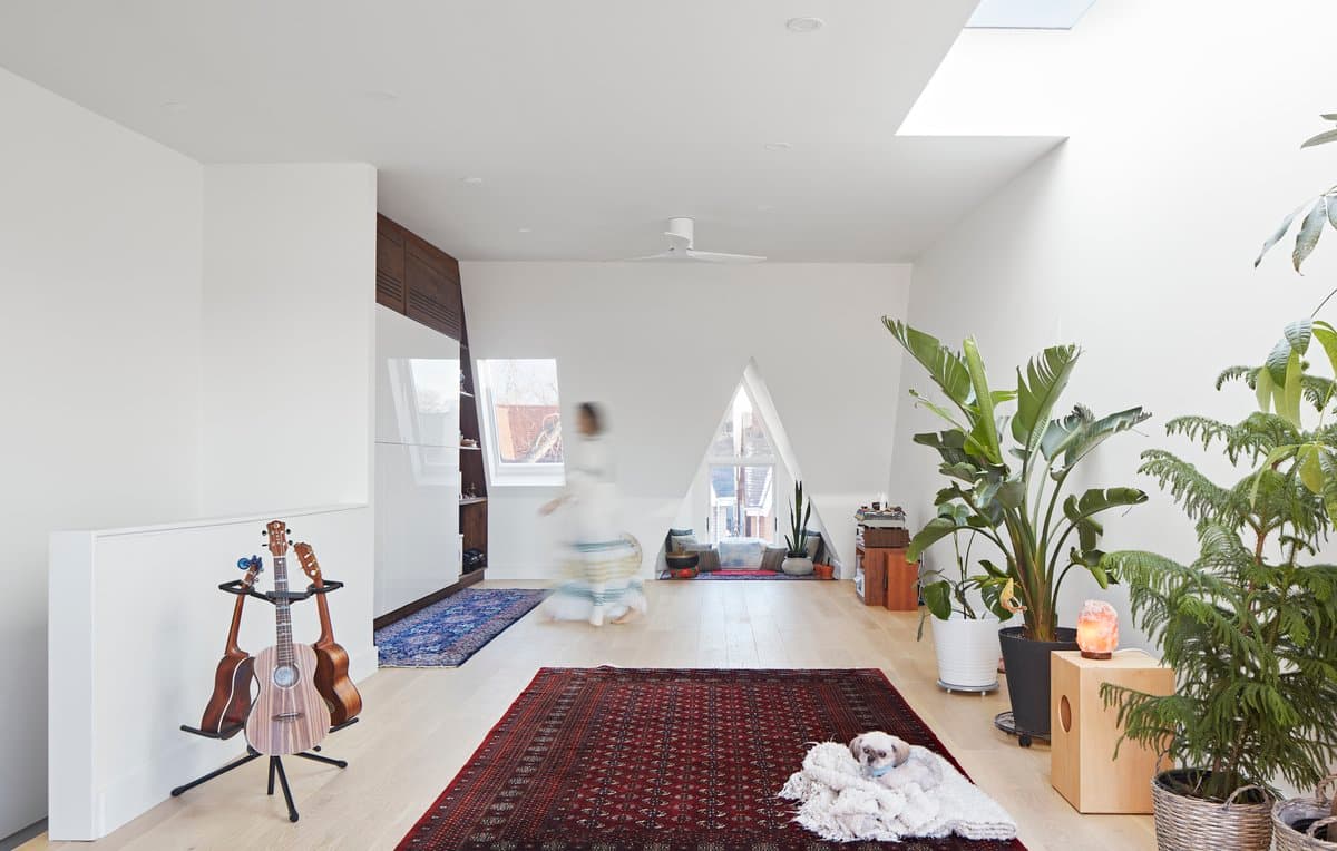 Minimalist room with skylights, guitars, cosy seating, rugs, and potted plants.