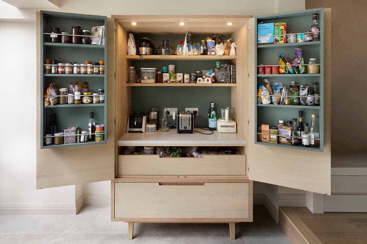 Meticulously organized pantry cupboard with various jars, bottles, and kitchen supplies in Wandsworth Cottage.