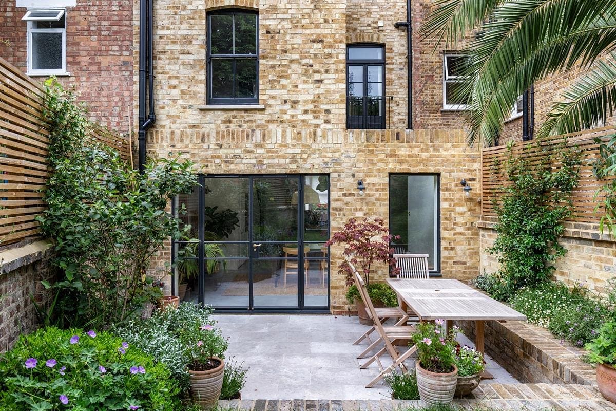 Inviting outdoor patio and garden featuring a wooden dining set and lush greenery.
