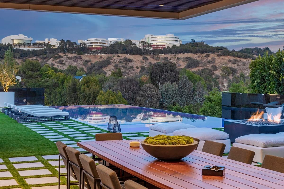 Luxurious outdoor living space with a wooden dining table, infinity pool, and serene landscaping.
