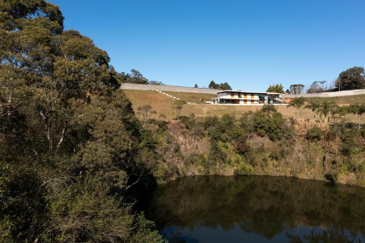 Modern building on a hill overlooking a tranquil pond with lush greenery.
