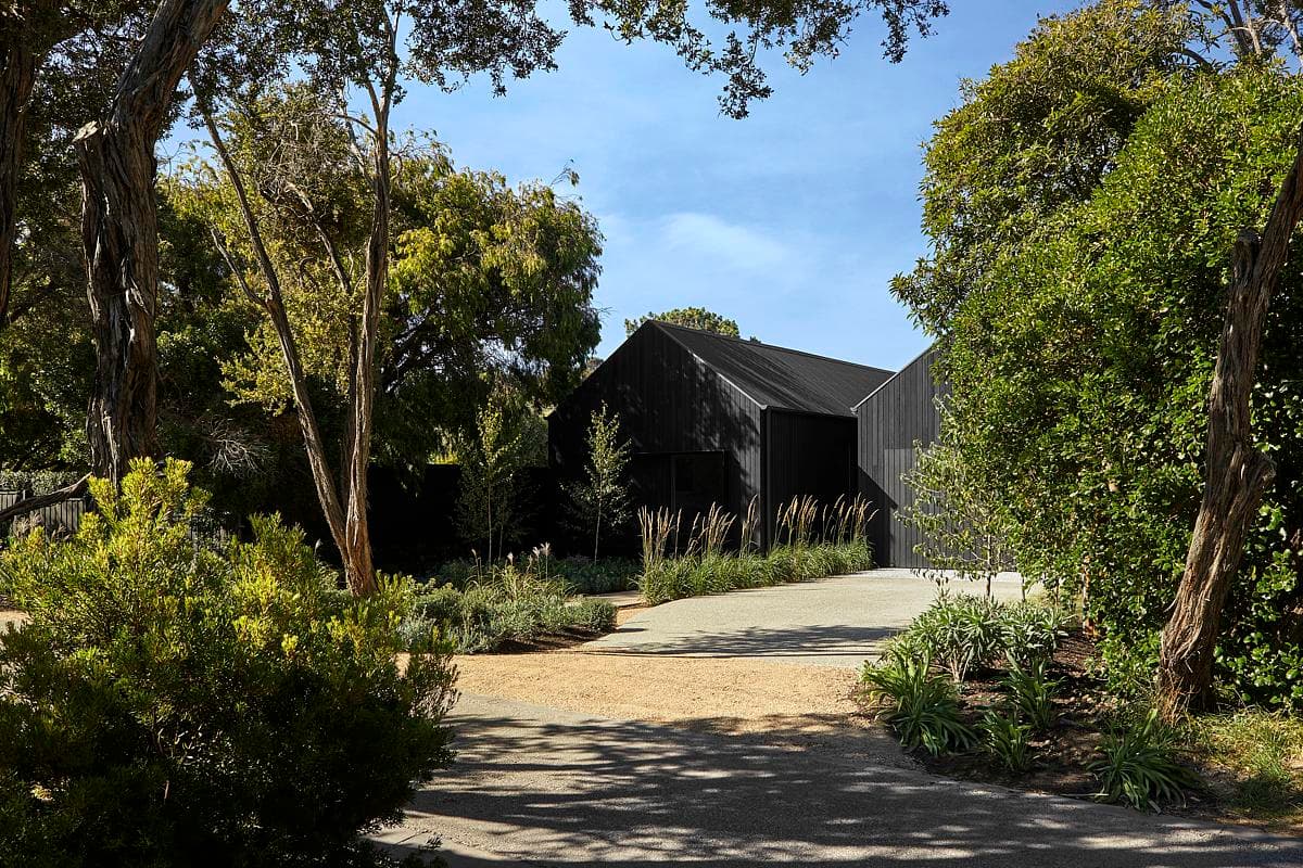 Contemporary black house set in vibrant greenery, blending modern design with nature’s beauty.