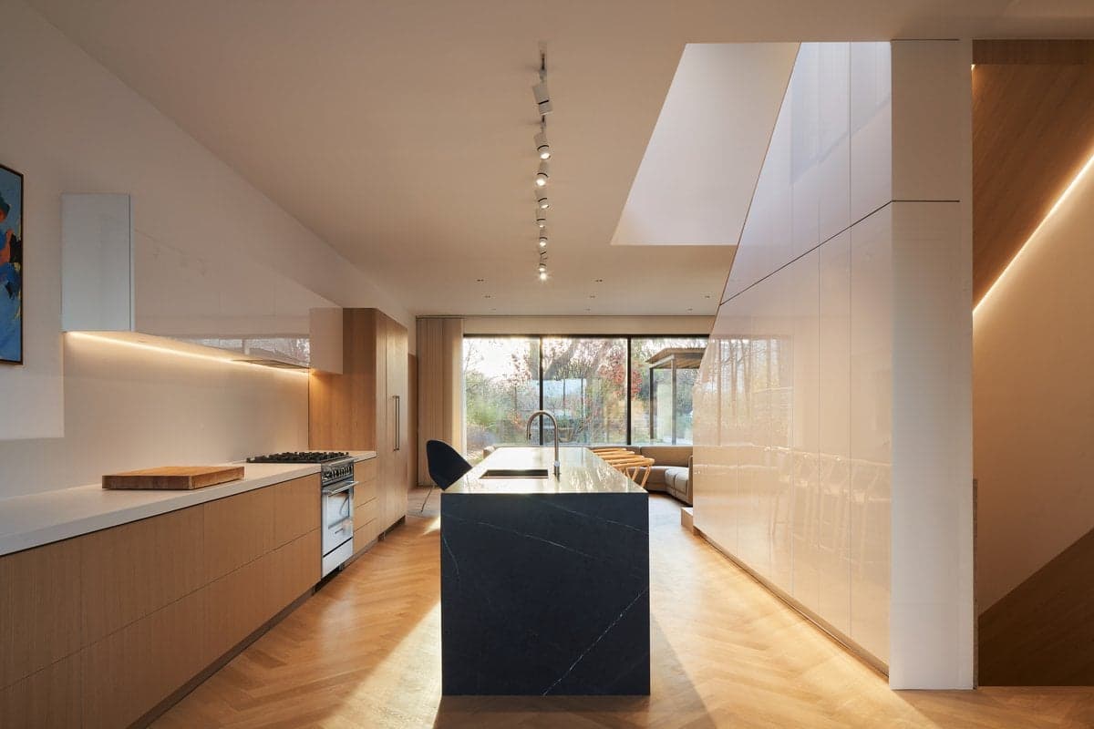 Modern minimalist kitchen with wood cabinetry, dark stone island, and large windows - Toronto residence.