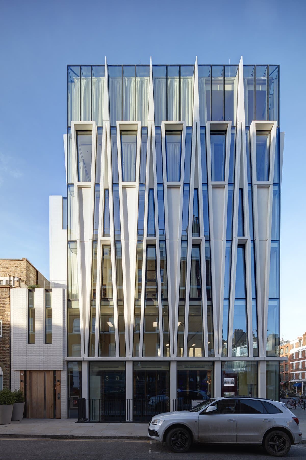 Modern multi-story building with glass facade, white framing, and large glass entrance.