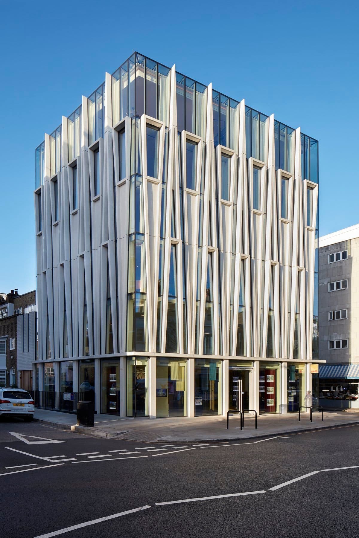 Modern multi-story building with glass facade and metal accents against a clear blue sky.