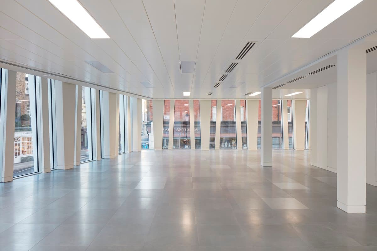 Spacious, modern office with polished floors, large windows, white walls, and ceiling panels.