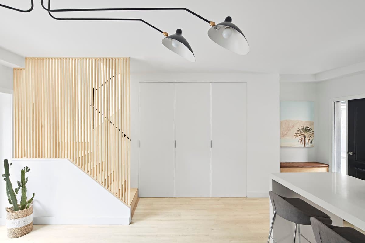 Modern minimalist interior with staircase, wooden slats, pendant lights, and cactus plant.