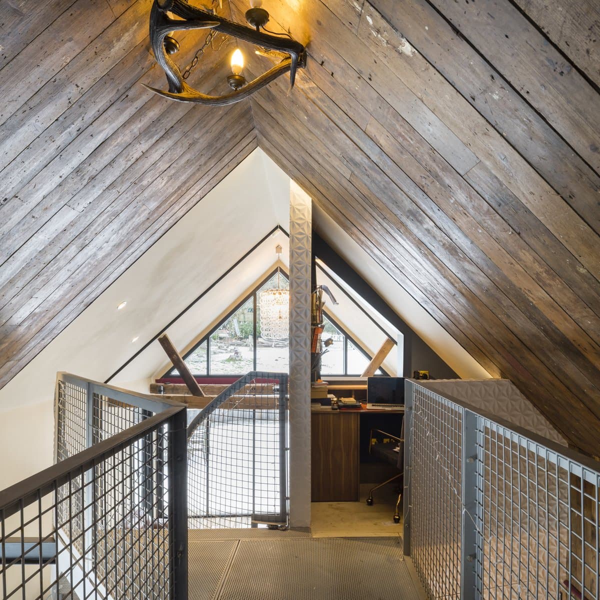 Rustic modern attic with wooden ceiling, antler chandelier, office, and natural light. Stanyards Cottage.