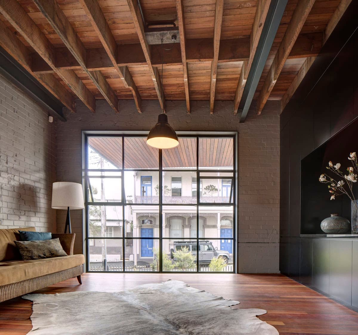 Cozy modern living room with industrial accents and natural light through large windows.