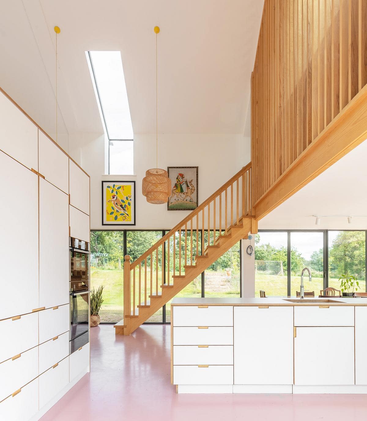 Timber staircase and balustrade above a pink floor, beside a tall window.