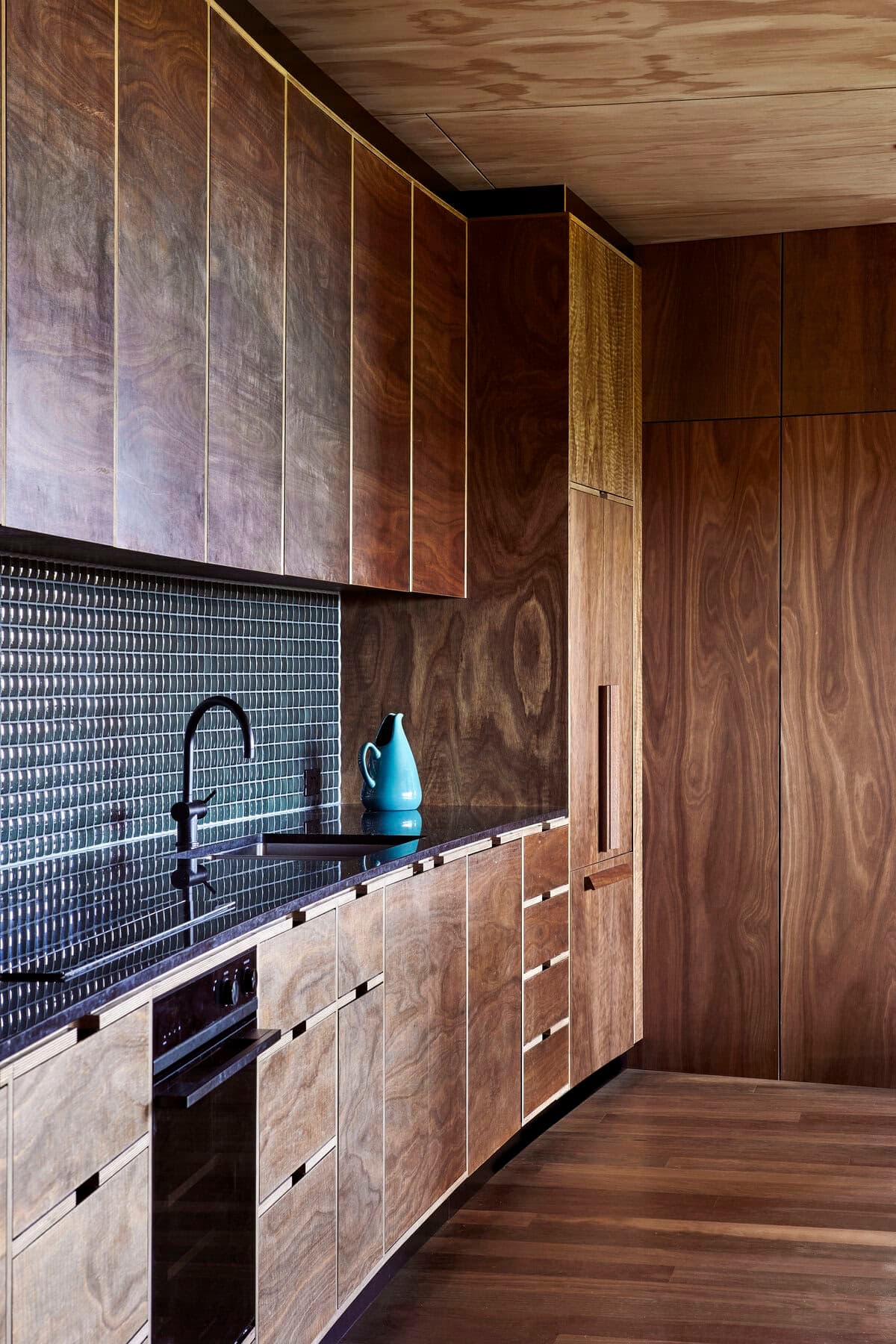 Chic minimalist kitchen featuring warm wood cabinetry and striking black countertop design.