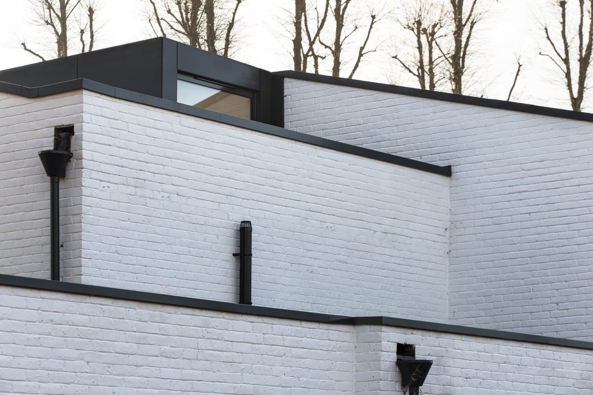 Modern white brick building with dark-framed windows and black fixtures, surrounded by leafless trees.