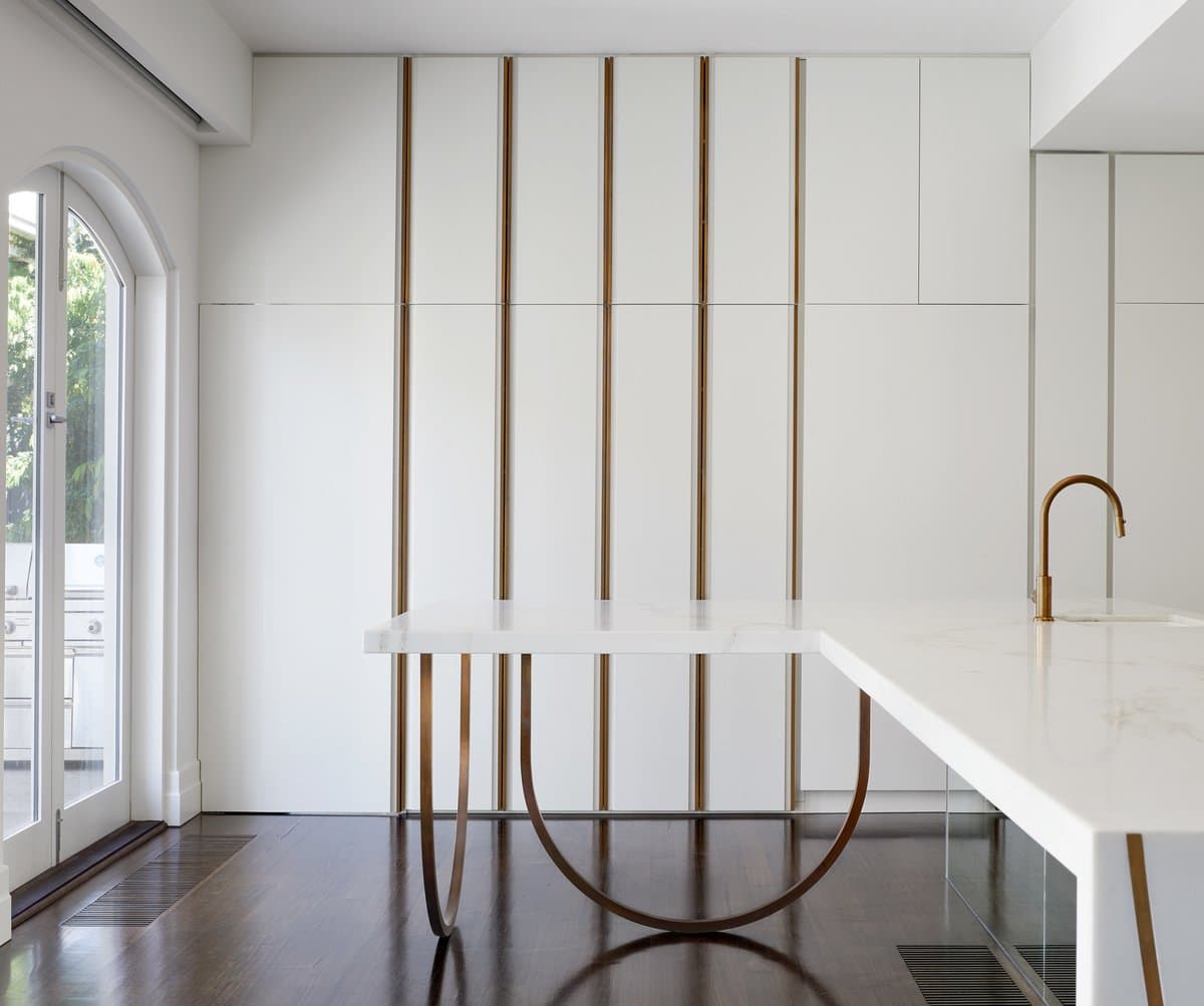 Modern white and gold minimalist kitchen with marble island and natural light.