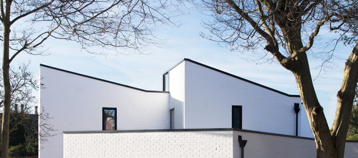 Modern minimalist white house with flat roof, large windows, and surrounding trees.