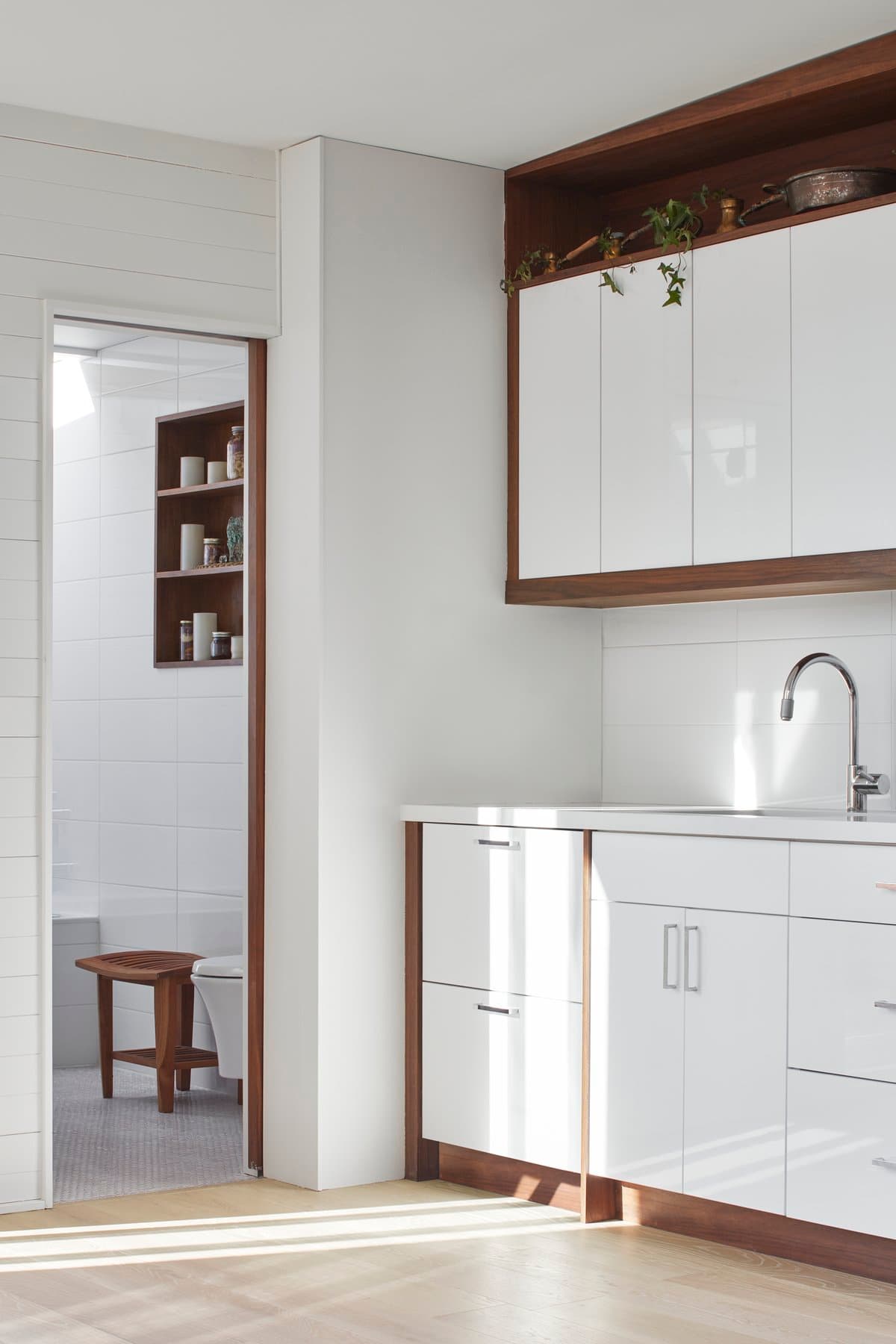Modern minimalist kitchen with white cabinetry, wood accents, and adjacent well-lit room.